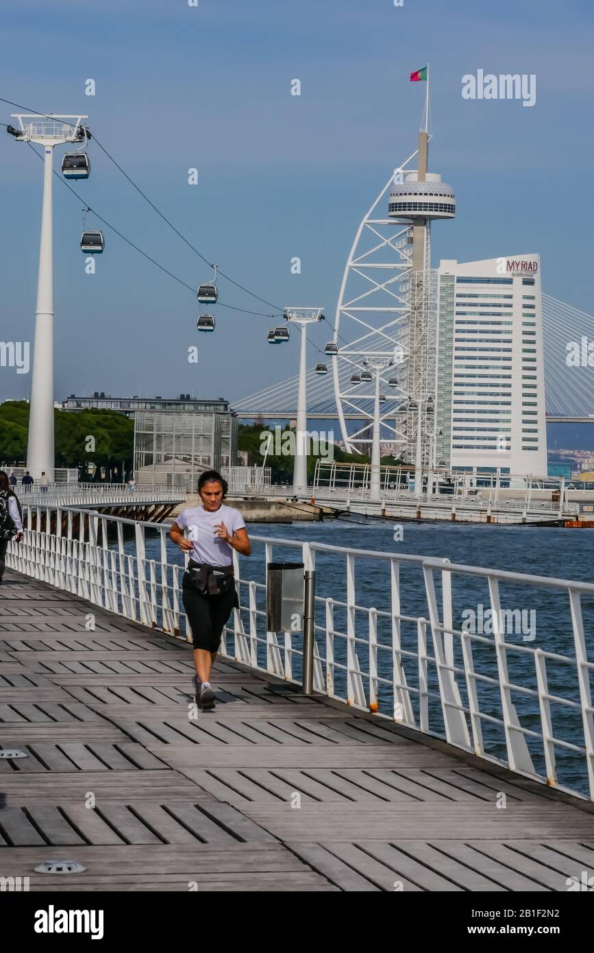 Una donna che corre lungo il ponte vicino all'acqua con la torre Vasco da Gama sullo sfondo in una giornata di sole a Lisbona Portogallo Foto Stock
