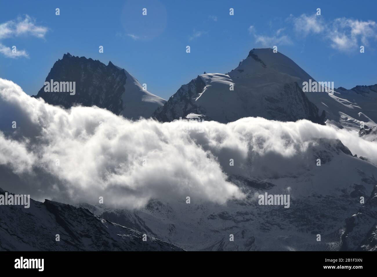 Nuvole basse intorno al Rimpfischhorn e Allalin in silhouette nelle Alpi svizzere meridionali sopra Saas Fee Foto Stock