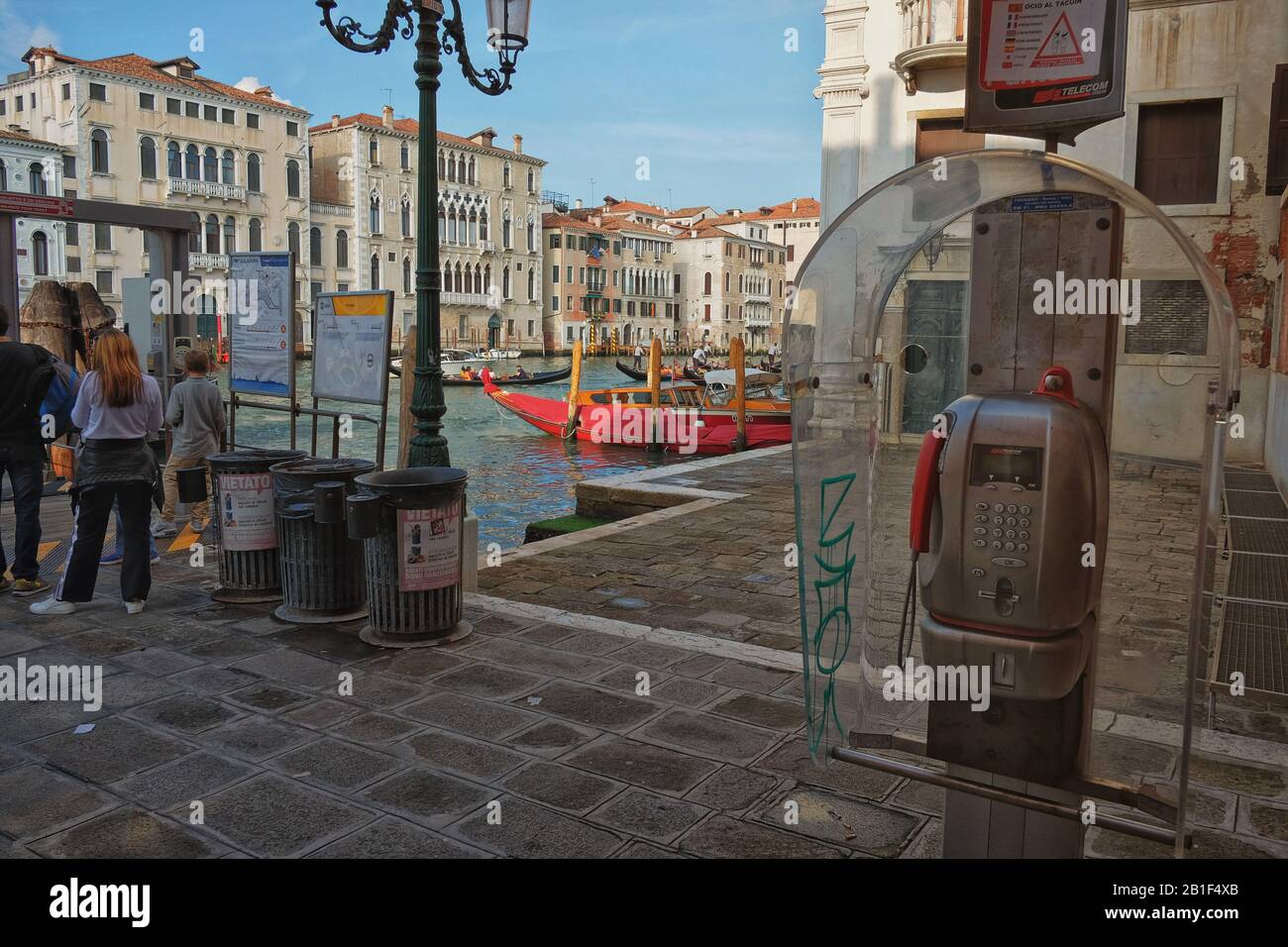 Un telefono pubblico a pagamento e alcuni bidoni dei rifiuti alla fermata del vaporetto Sant'Angelo sul Canal Grande, gondole e Palazzo al pomeriggio luce, Venezia Italia Foto Stock