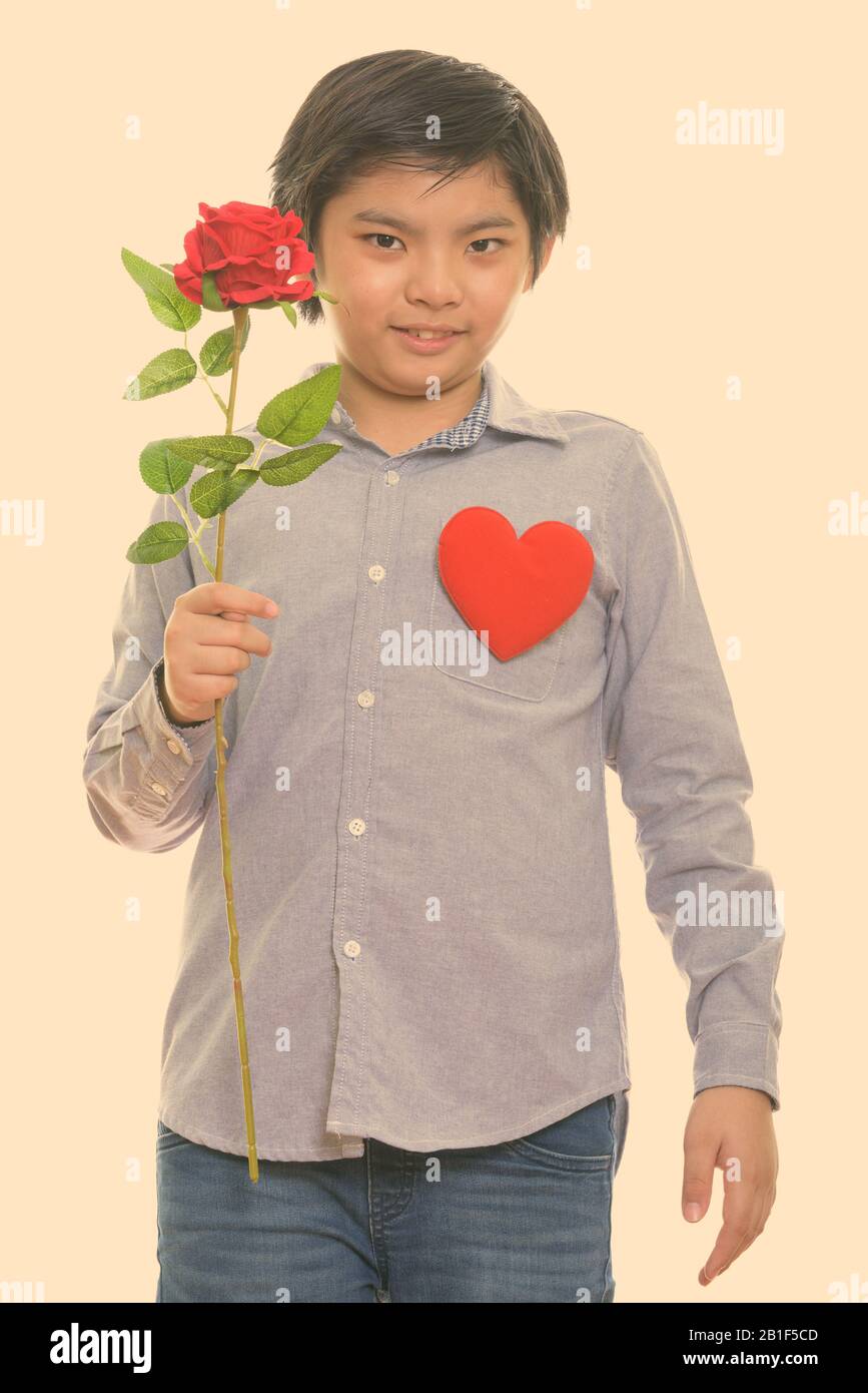 Studio shot di carino ragazzo giapponese tenendo una rosa rossa con cuore rosso sul petto Foto Stock