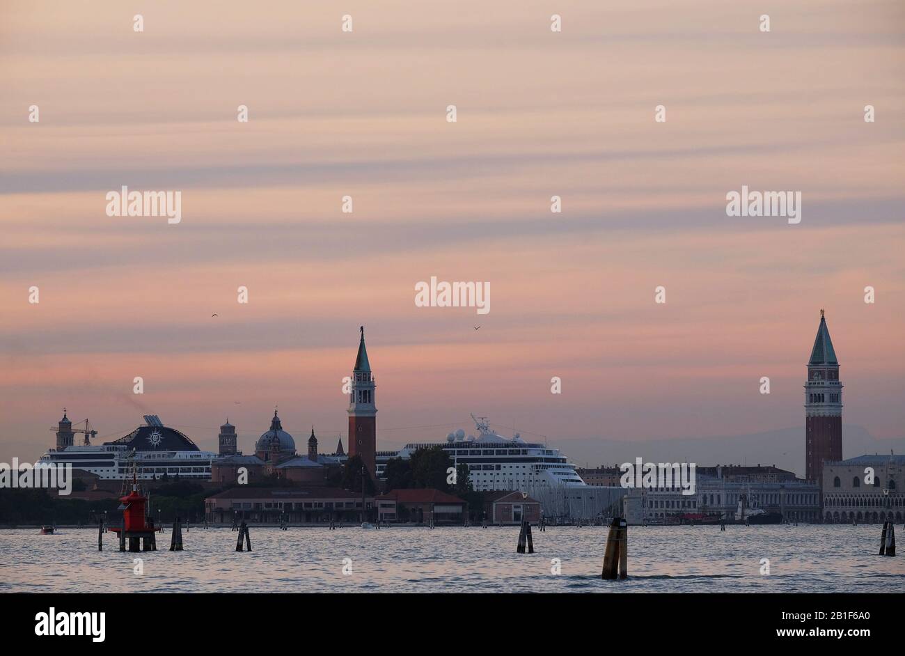 Una grande nave da crociera domina lo skyline di Venezia, lasciando il canale della Giudecca che sovrasta le cupole di San Giorgio maggiore, viste dal Lido attraverso il bacino di San Marco Foto Stock