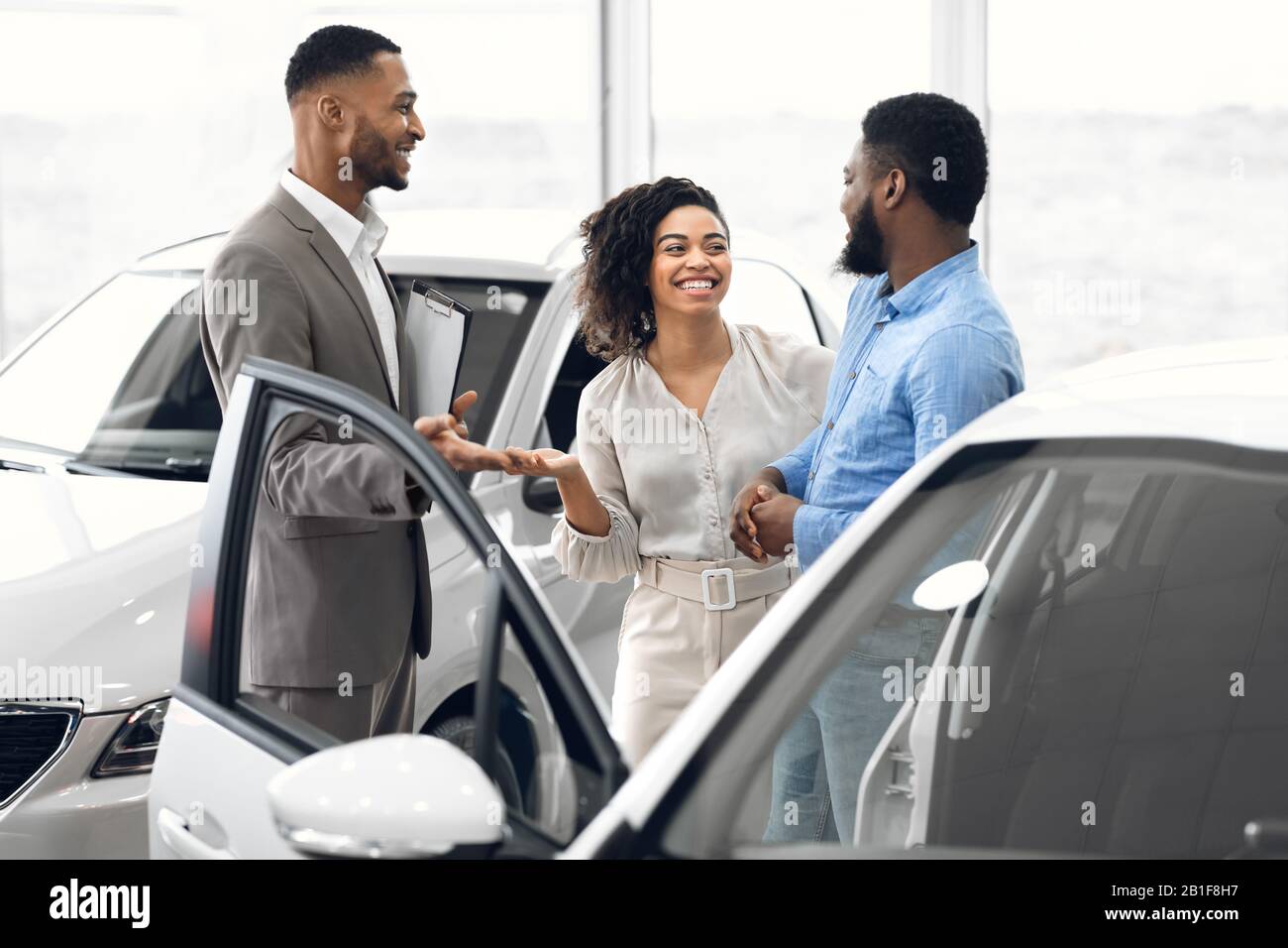 Manager Che Parla Con Gli Acquirenti Che Acquistano Auto In Piedi Nel Dealership Shop Foto Stock