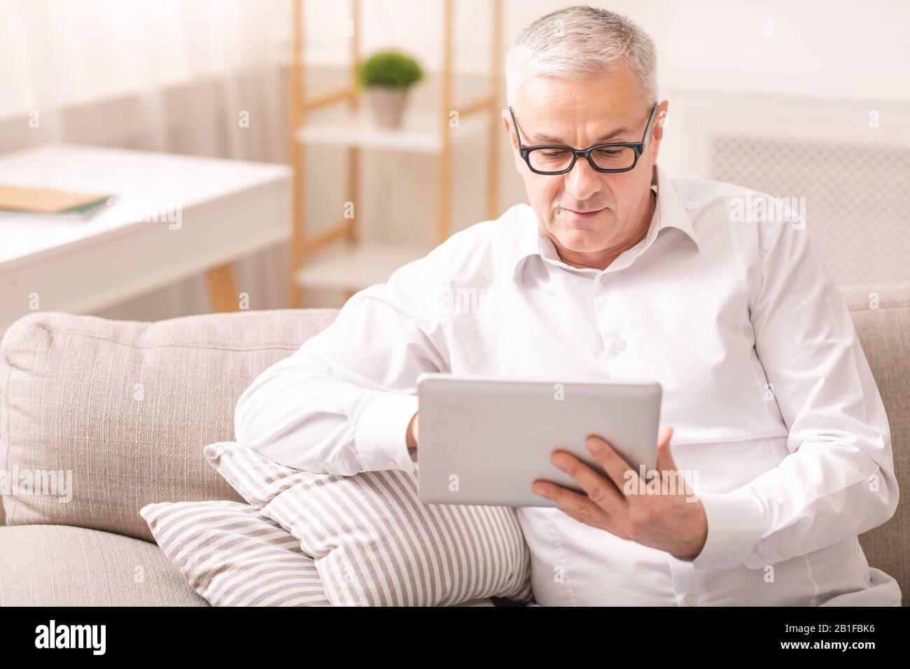 Uomo anziano che usa un tablet digitale seduto sul divano Foto Stock
