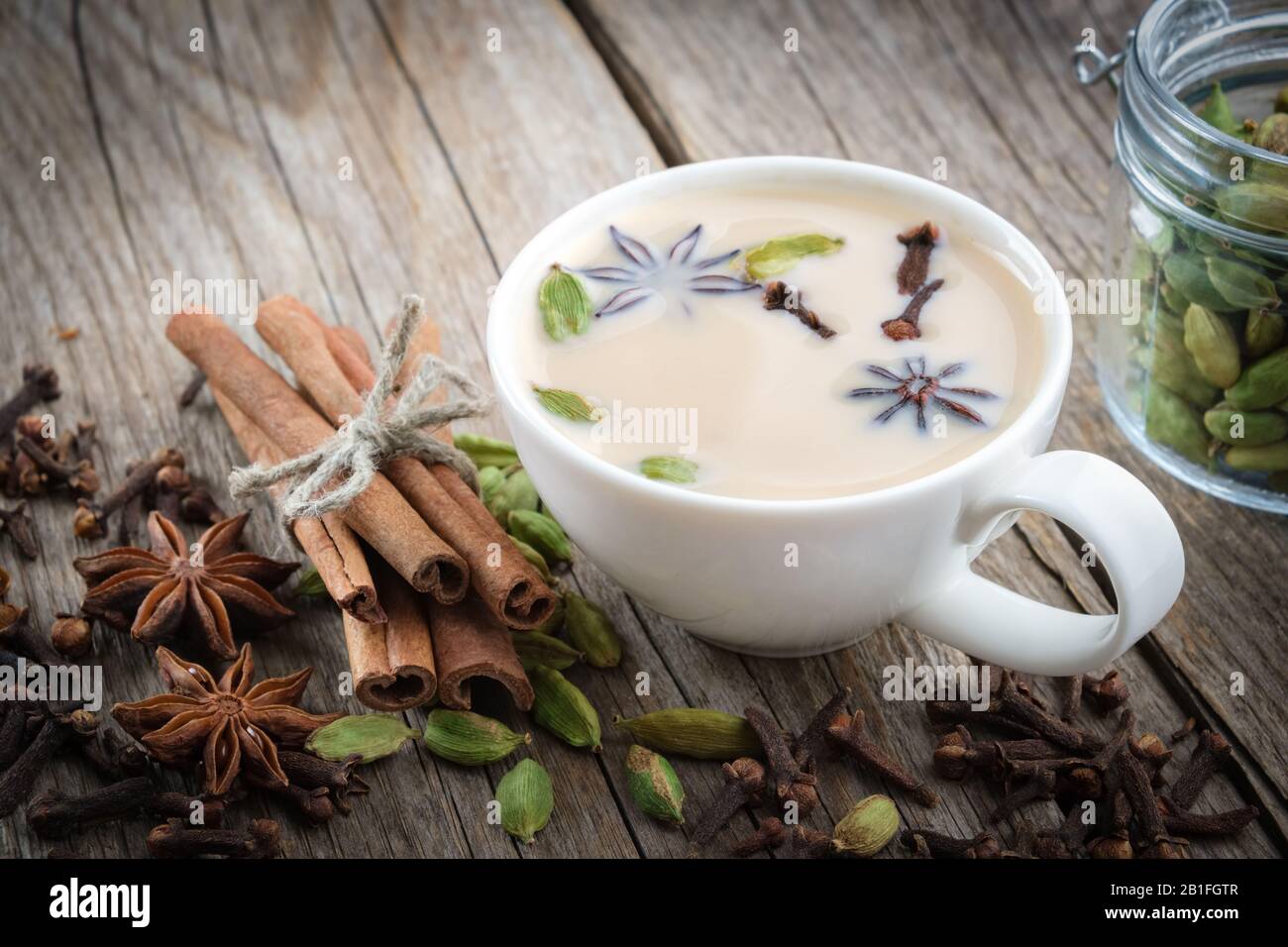 Tazza di sano tè ayurvedico masala o caffè con latte e spezie aromatiche. Bastoncini di cannella, baccelli di cardamomo, chiodi di garofano e stelle anice su tavola di legno. Foto Stock