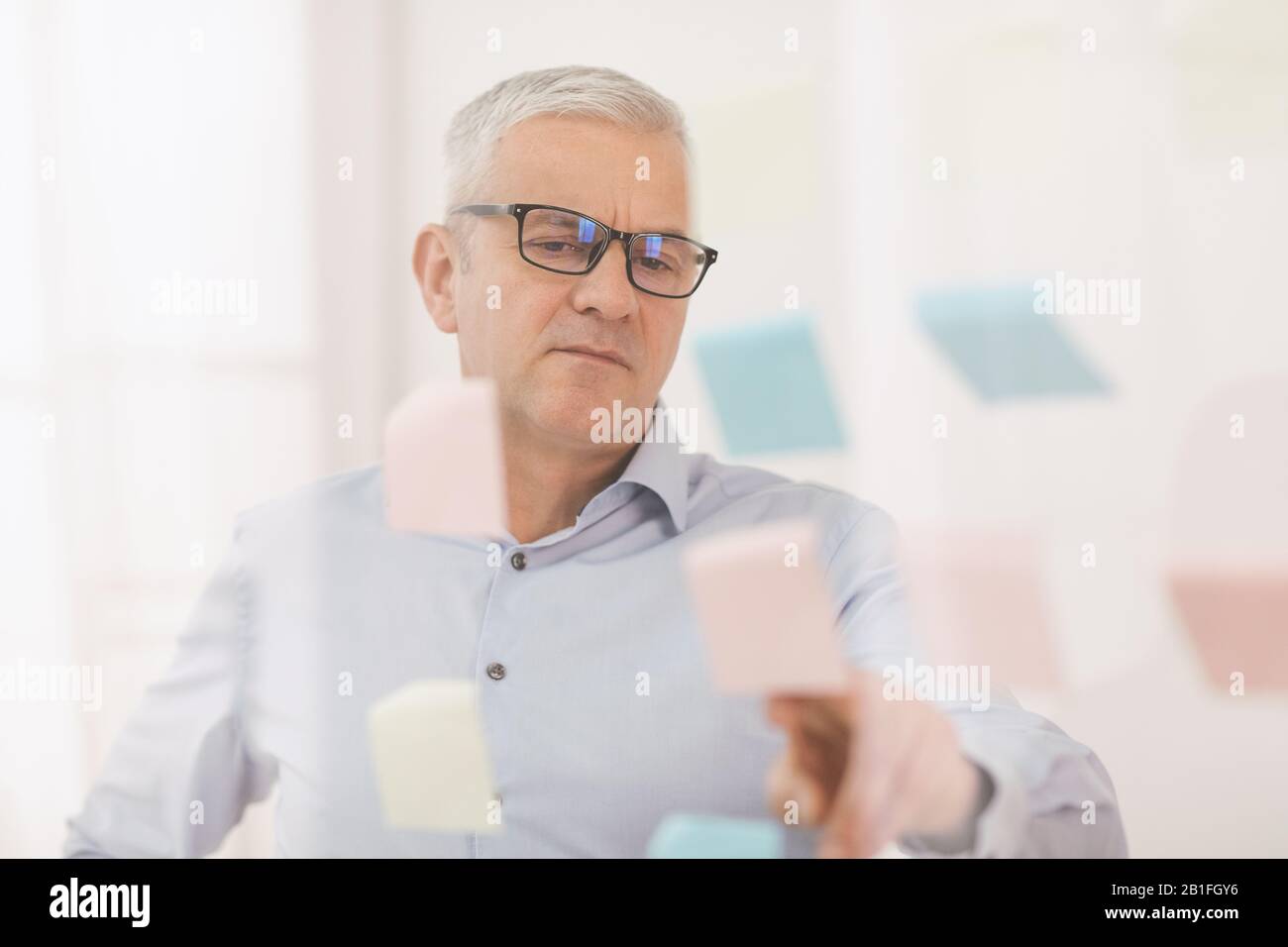 Responsabile anziani che mette le note adesive sulla finestra Foto Stock