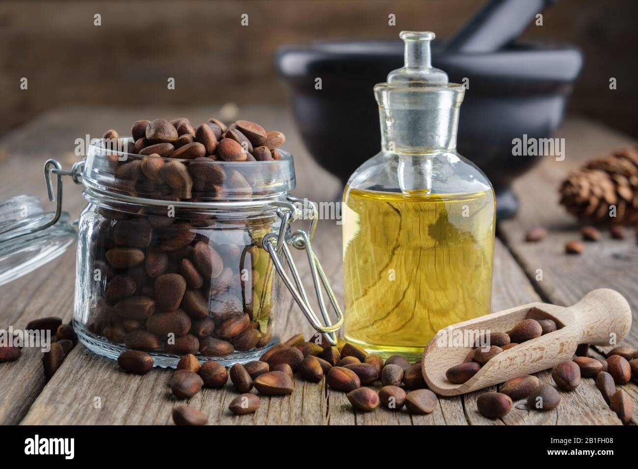 Vaso di pinoli e pinoli bottiglia d'olio essenziale. Mortaio nero su sfondo. Foto Stock