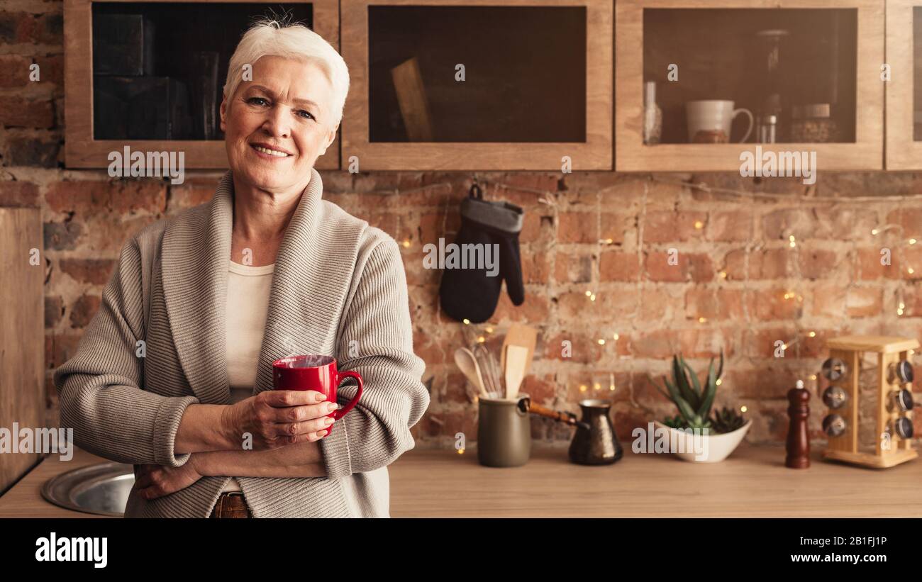 Donna Anziana Rilassata Con Tazza Di Caffè In Posa In Cucina Foto Stock