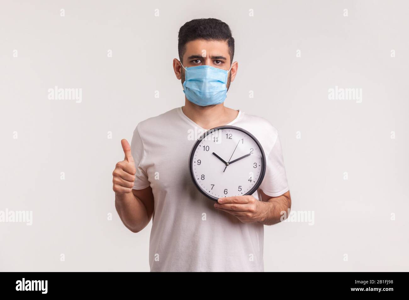 Tempo di combattere il coronavirus. Uomo in maschera igienica protettiva che tiene orologio, avvertimento di nuova epidemia di virus, quarantena e rischio durante l'incubazione perio Foto Stock