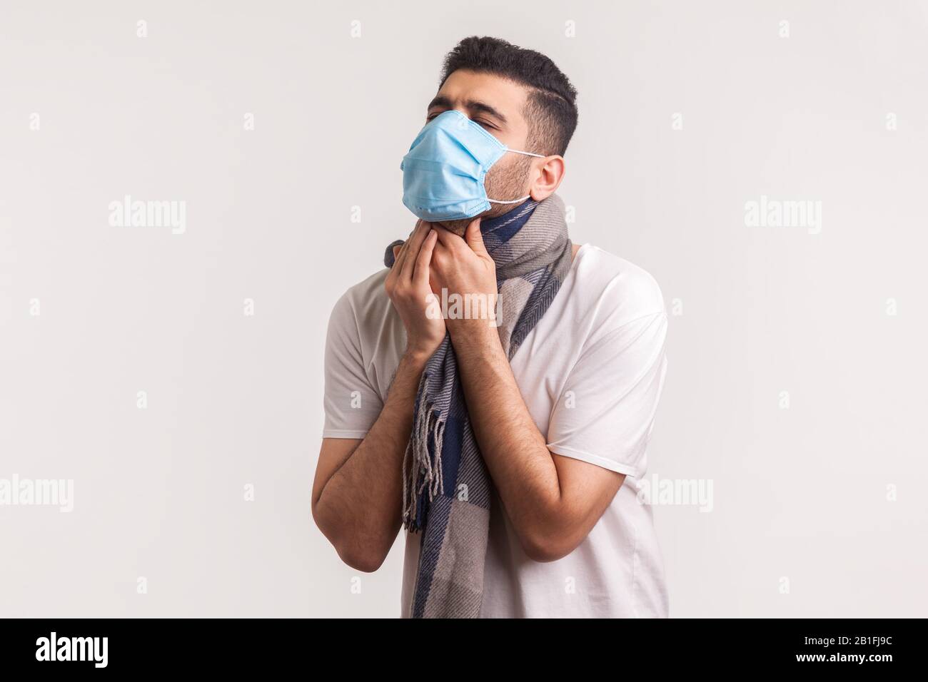 Uomo con maschera igienica e sciarpa che soffre di mal di gola, tosse e soffocamento, con sintomi di influenza, infezione contagiosa da coronavirus 2019-nCoV. In Foto Stock