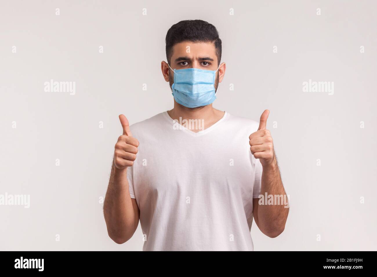Protezione efficace contro le malattie contagiose. L'uomo che mostra i pollici e indossa una maschera igienica per prevenire infezioni, malattie respiratorie come l'influenza Foto Stock