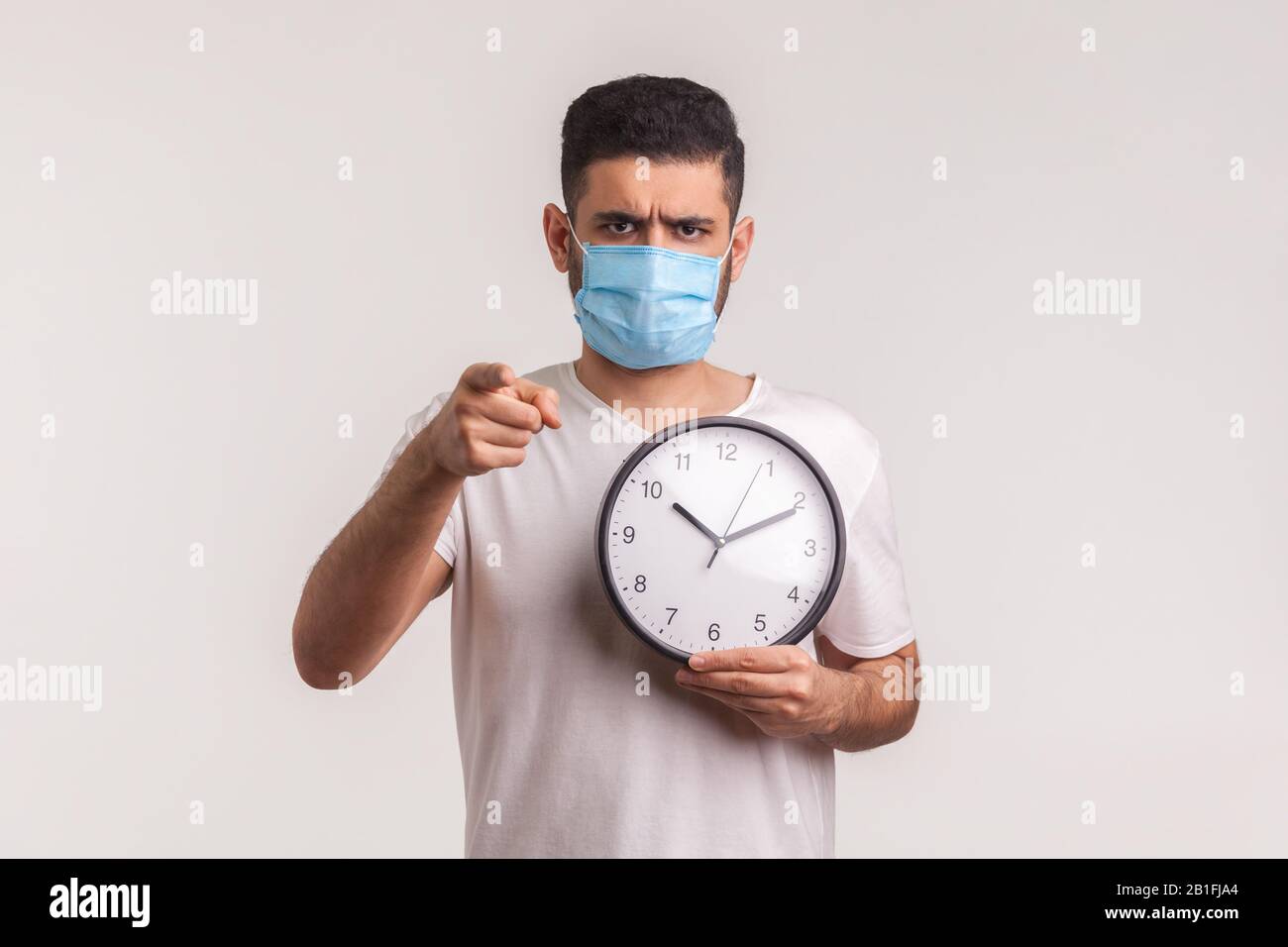 È il momento di essere cauti! Uomo in maschera igienica protettiva che tiene orologio, avvertimento di nuova epidemia di virus, quarantena e rischio durante il periodo di incubazione. IND Foto Stock