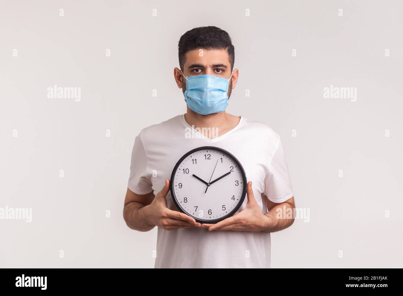 Tempo per fermare il coronavirus. Uomo in maschera igienica protettiva che tiene orologio, avvertimento di nuova epidemia di virus, quarantena e rischio durante il periodo di incubazione Foto Stock
