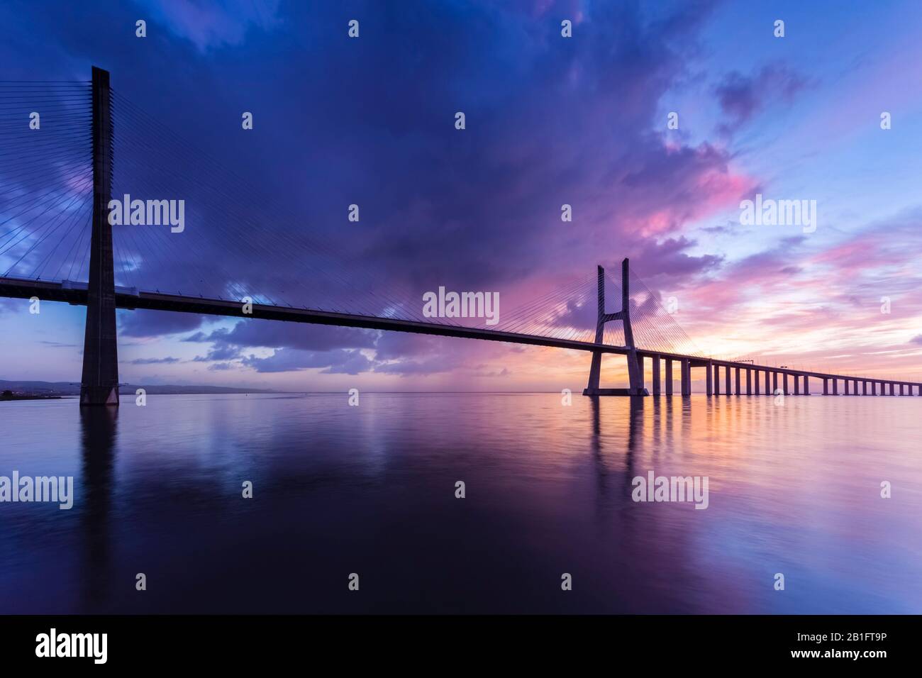 Un'alba colorata dietro il ponte Vasco da Gama, riflessa sul fiume Tago. Lisbona, Portogallo, Europa. Foto Stock