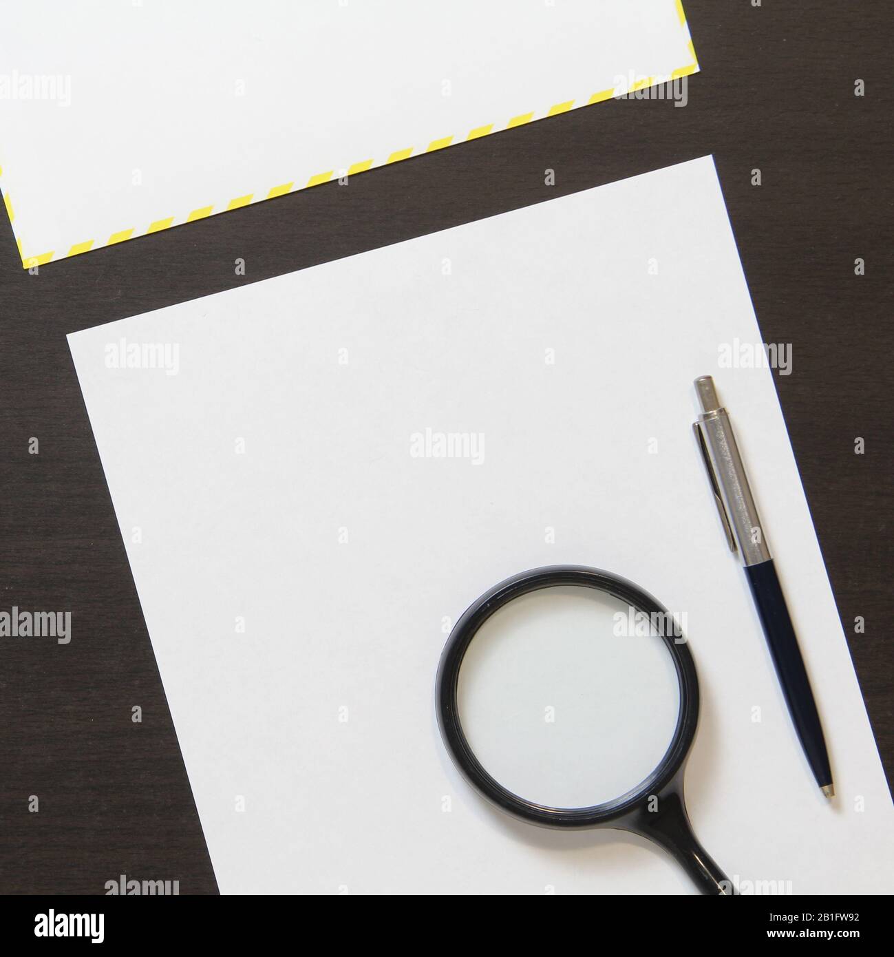 Modello di carta bianca con penna, busta e lente di ingrandimento su sfondo di legno di color wenge scuro. Concetto di business plan, ricerca, rilevamento e risoluzione dei problemi. Con spazio vuoto per il testo. Foto Stock
