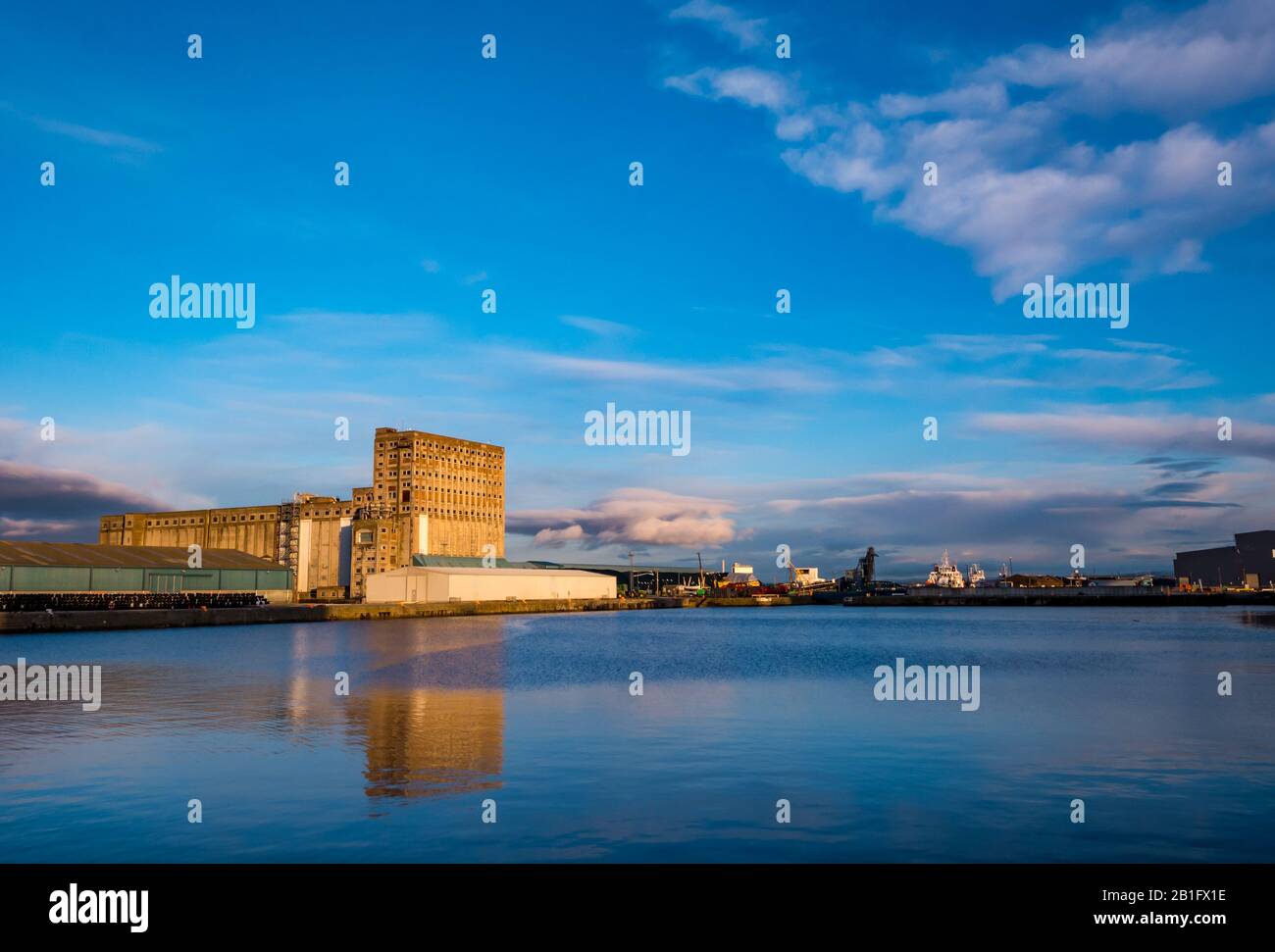 Leith, Edimburgo, Scozia, Regno Unito. 25 Feb 2020. Regno Unito Meteo: Il sole al crepuscolo illumina un grande edificio industriale di silo granulare che si riflette nell'acqua di Imperial Dock, porto di Leith Foto Stock