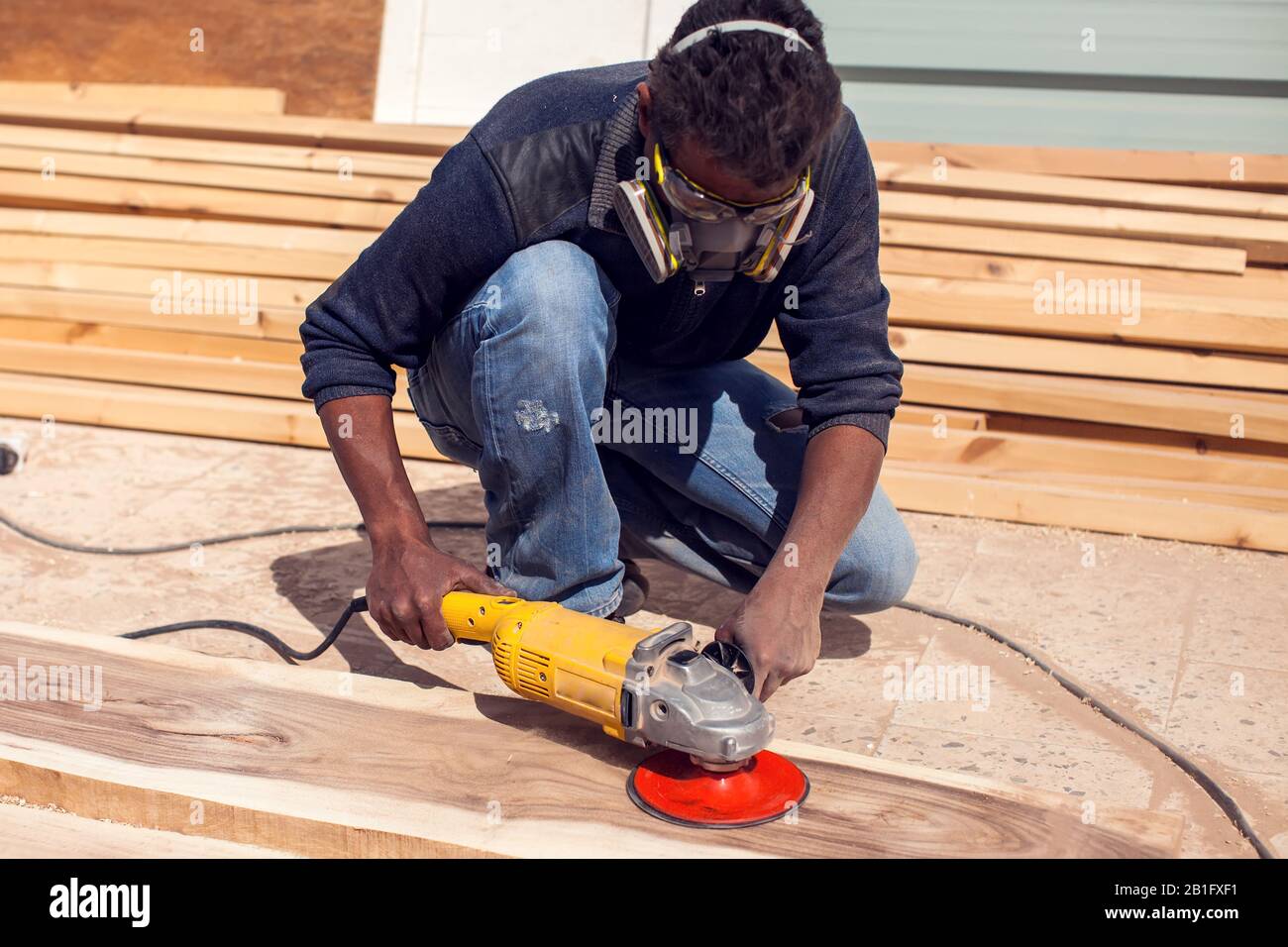 Un uomo a mano in maschera lucidante legno Plank esterno. Foto Stock