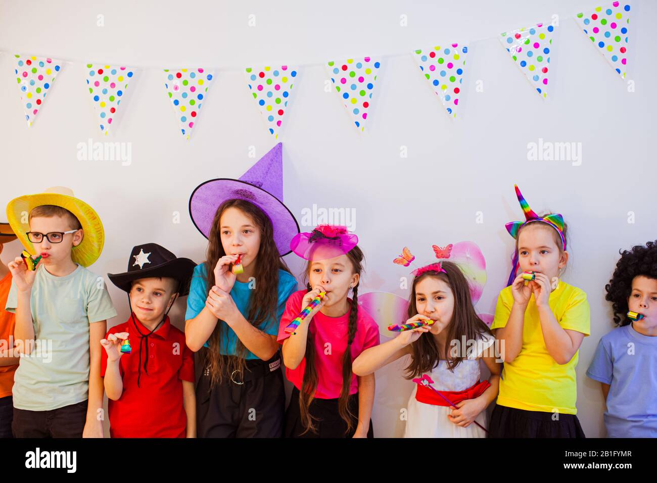 I bambini gioiosi felici celebrano il compleanno e indossano i cappucci divertenti della festa. I bambini sono carini e si sono sibilati Foto Stock