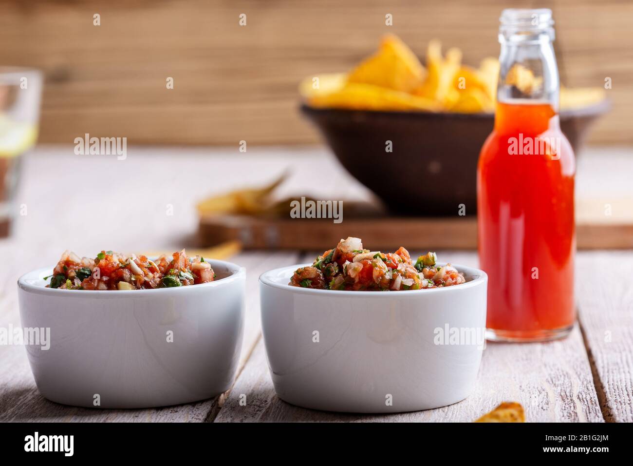 Due ciotole piene di salsa, salsa calda al peperoncino rosso bottiglia e tortilla chip su rustico tavolo di legno Foto Stock