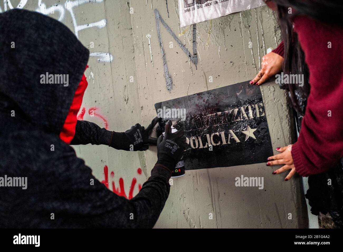 Uno spray studentesco radicale dipinge uno slogan politico sul muro durante una marcia di protesta contro le politiche del governo a Bogotá, Colombia. Foto Stock
