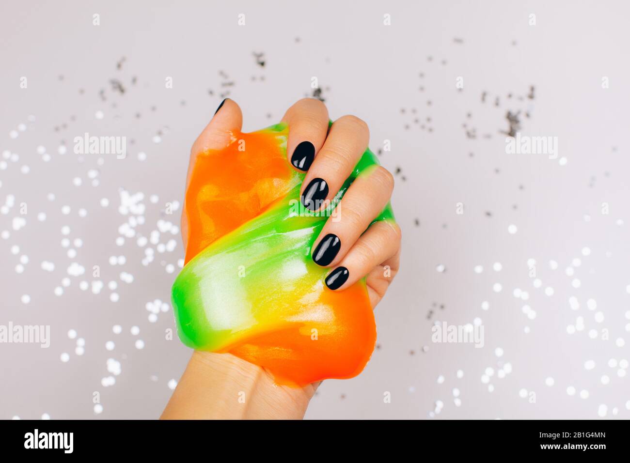 mani con manicure nero che tiene la calce in arancione e verde vibrante colori Foto Stock