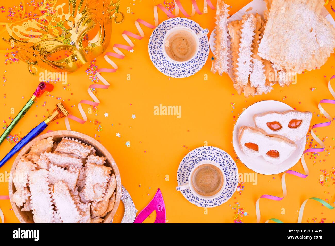 Maschera di Carnevale, due tazze di caffè aromatico, dolci e confetti su sfondo giallo. Decorazioni per una tradizionale vacanza italiana. Spazio di copia. Disposizione piatta. Foto Stock