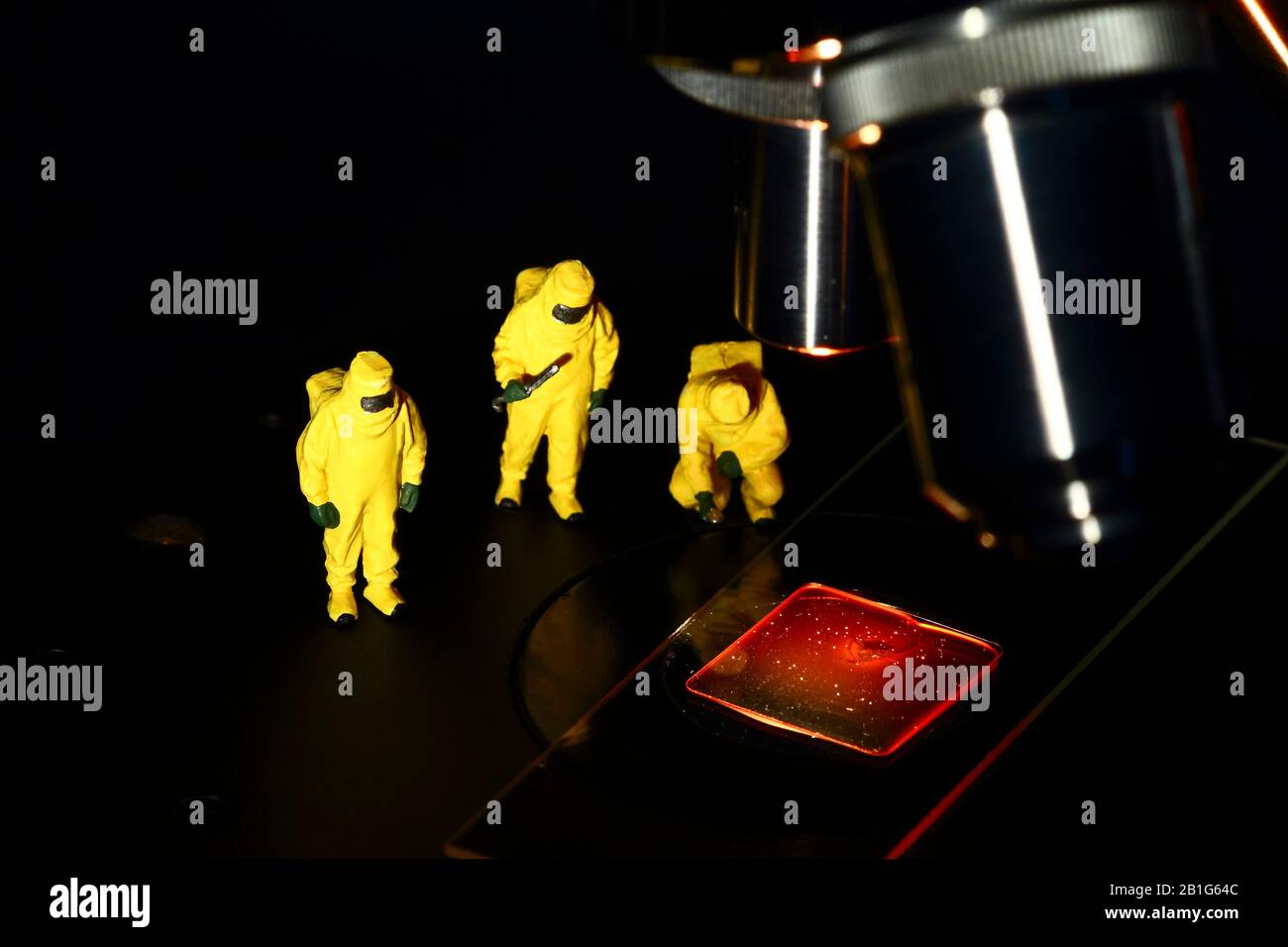 Immagine concettuale della figura in miniatura persone che indossano abiti Hazmat guardando un campione di sangue falso sotto un microscopio Foto Stock
