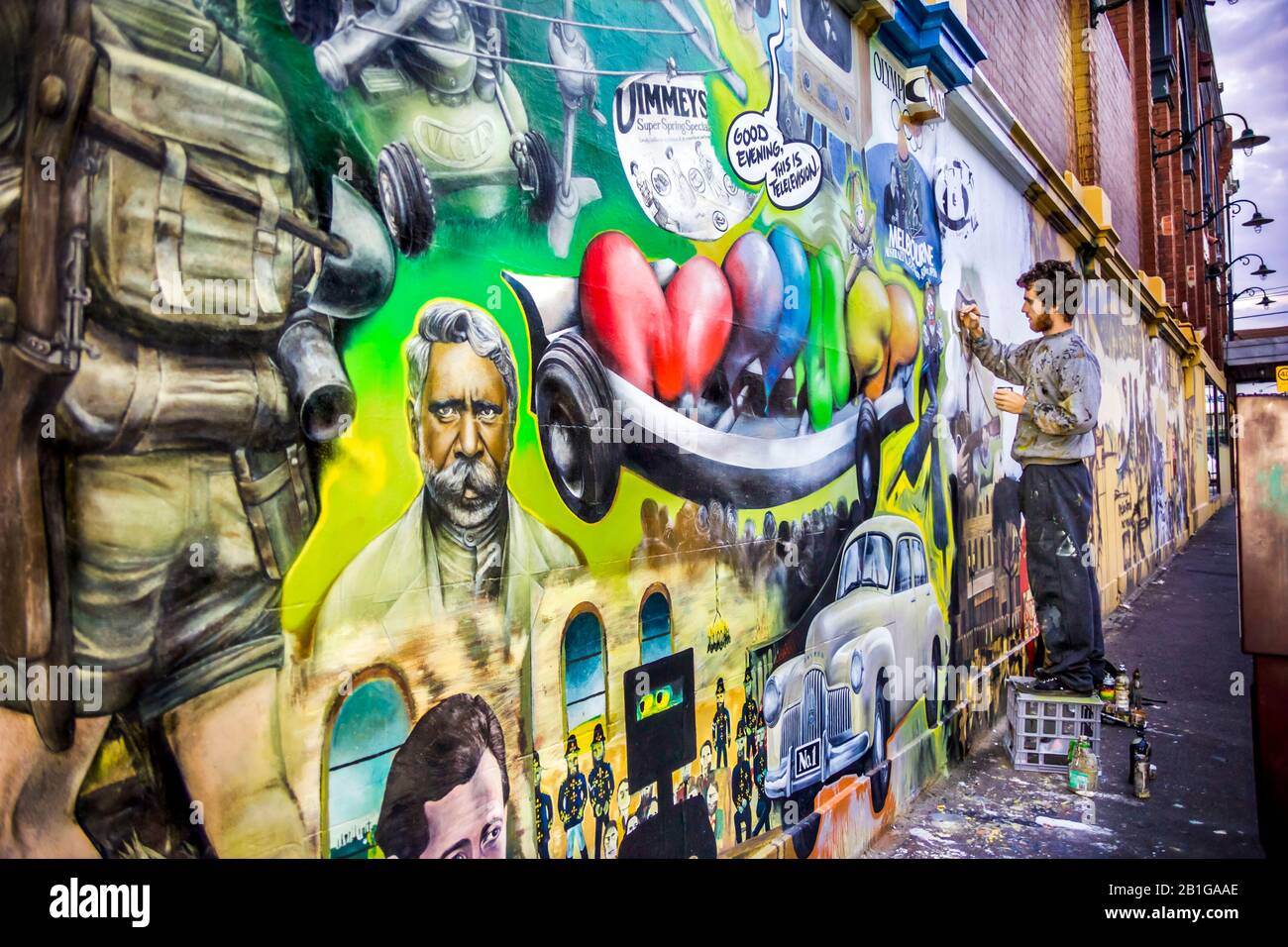 Young man, artista al lavoro che dipinge un murale raffigurante i temi simbolo di Melbourne, Richmond, Melbourne, Victoria, Australia Foto Stock