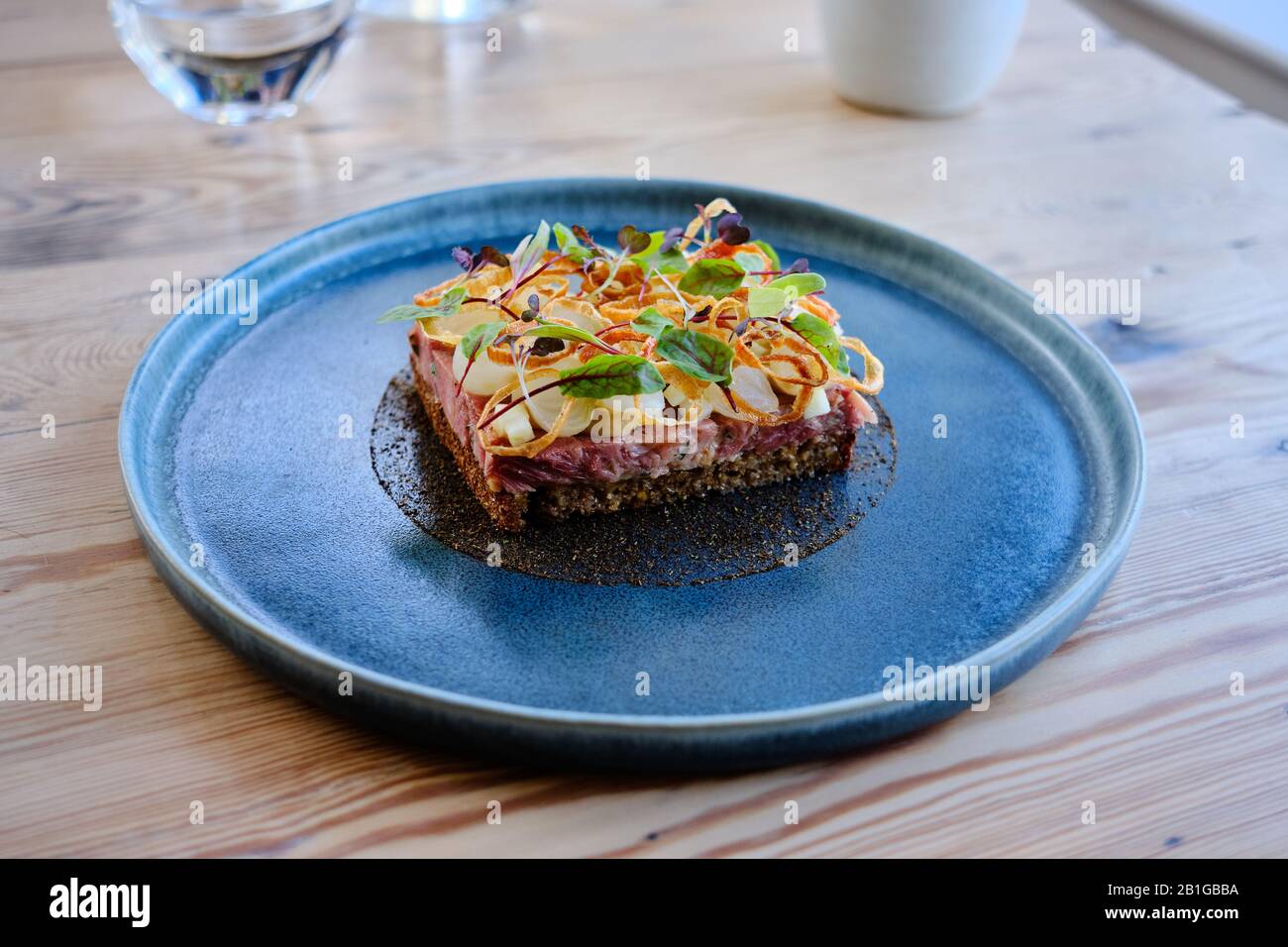 Un tradizionale panino aperto di maiale tirato con mela, anelli di cipolla fritti e foglie in stile scandinavo Foto Stock