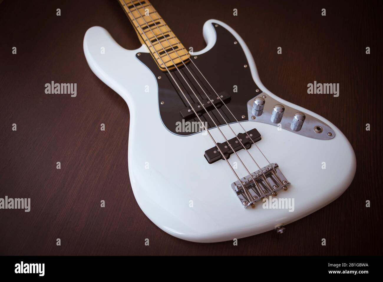 Chitarre White Electric Bass Con Collo D'Acero, Sottaceti Neri E Inserti Black Block Su Un Semplice Sfondo In Legno Foto Stock