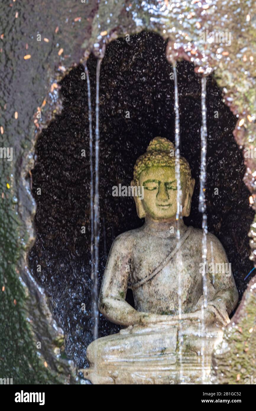 un dio buddista buddha o divinità in una grotta di pietra con una cascata e acqua corrente che cade dalle rocce in thailandia, asia. Foto Stock