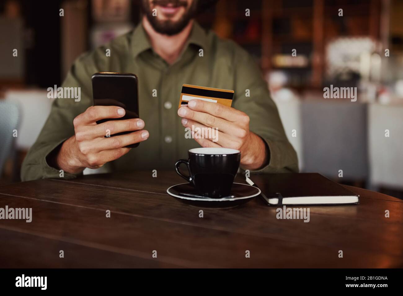 Closeup di allegro uomo caucasico mano che tiene il telefono cellulare digitando i dettagli della carta per effettuare il pagamento online seduto in caffetteria Foto Stock