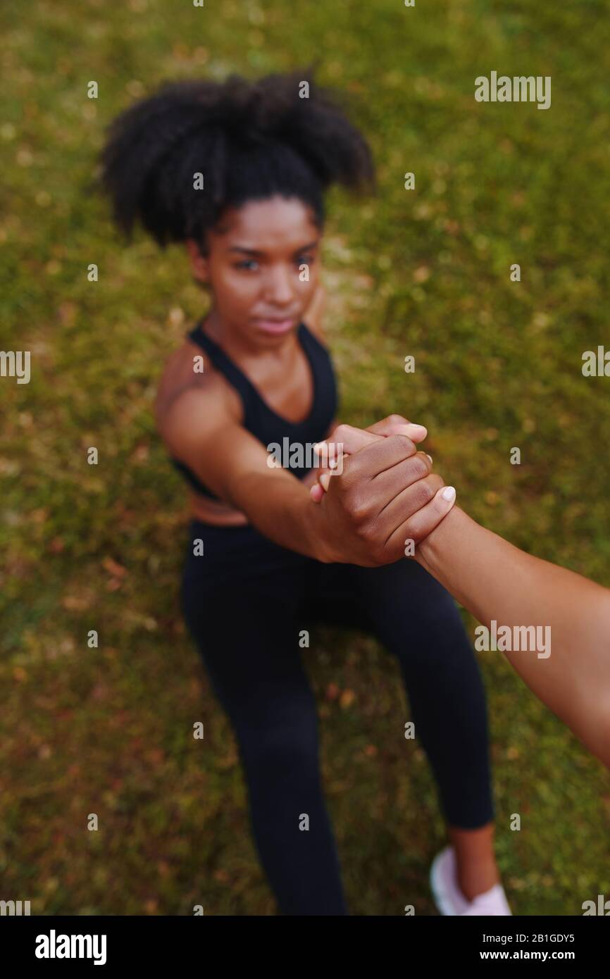 amici che danno una mano d'aiuto ad una giovane donna africana americana di idoneità per ottenere in su dal terreno dopo l'esercitazione Foto Stock