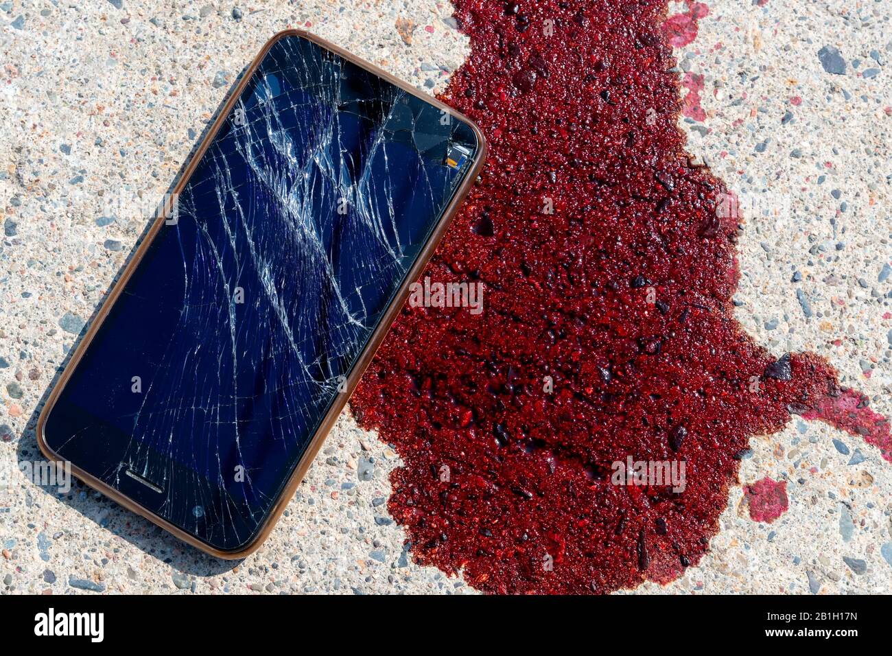 Un telefono cellulare rotto e rotto da una pozza di sangue su un marciapiede. Lo schermo del telefono cellulare è rotto e frantumato. Il sangue è fresco. Foto Stock