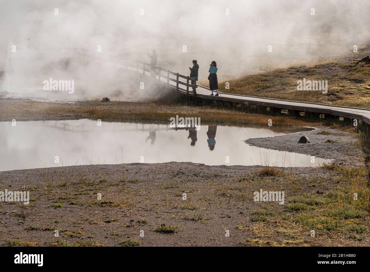 Turisti su passerella in legno che guarda alle sorgenti termali calde fumanti nella nebbia. Foto Stock