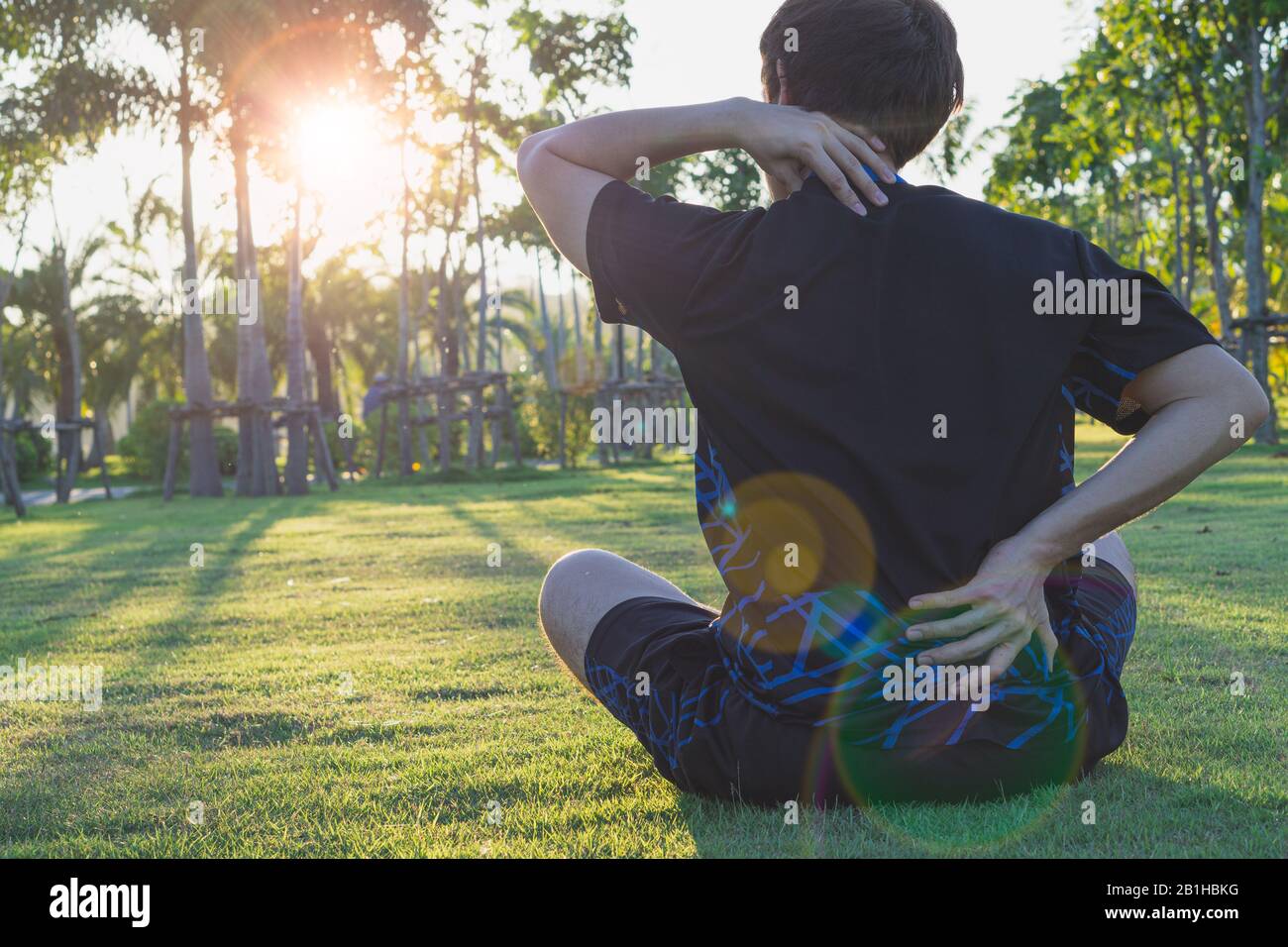Un atleta maschio che soffrono di dolori al collo e alla schiena e di pregiudizio al parco. Lo sport e il concetto di assistenza sanitaria. Foto Stock