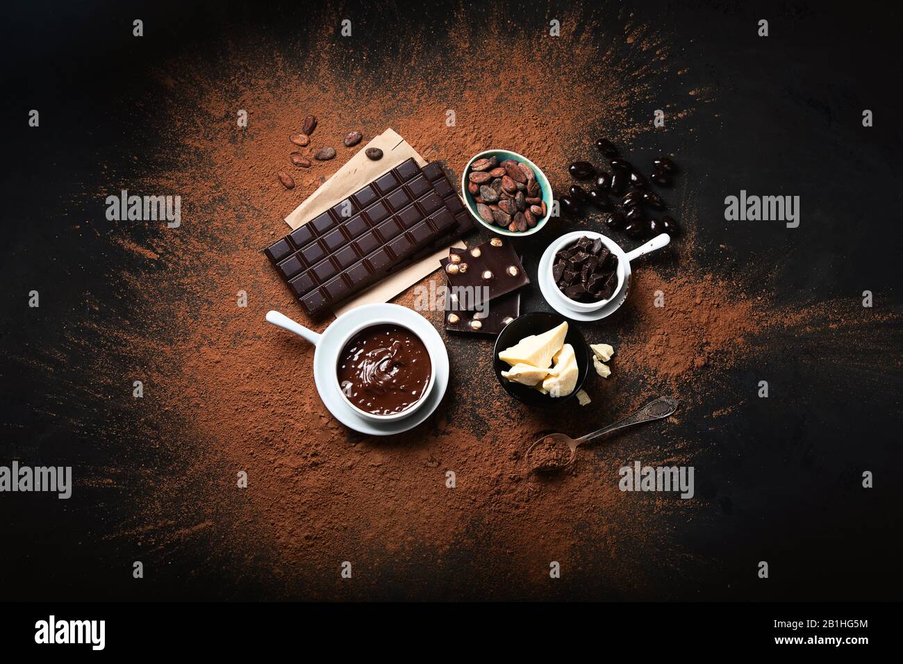 Barra di cioccolato fondente, pezzi di cioccolato e fave di cacao, polvere di cacao su sfondo nero. Vista dall'alto Foto Stock