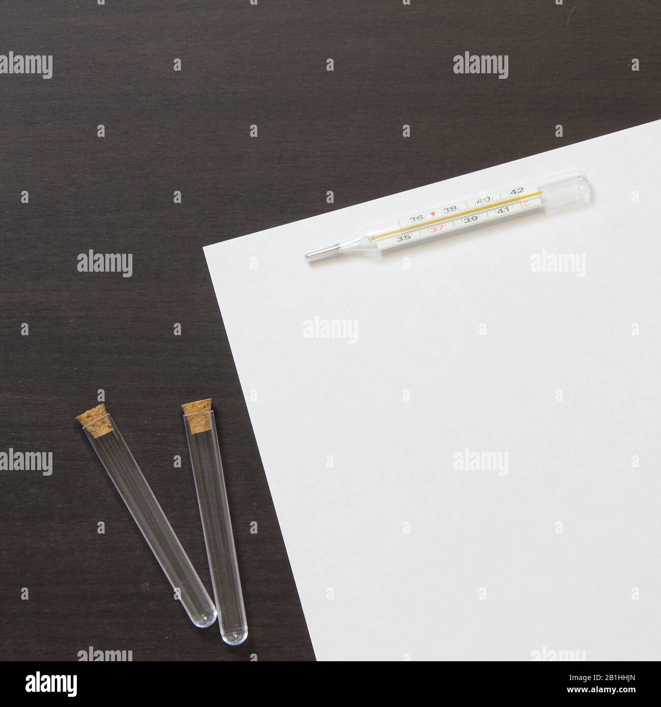Modello di carta bianca con termometro e bottiglia su fondo in legno di colore wenge scuro. La fornitura di servizi medici e farmacologici. Stock foto con spazio vuoto per testo e design Foto Stock