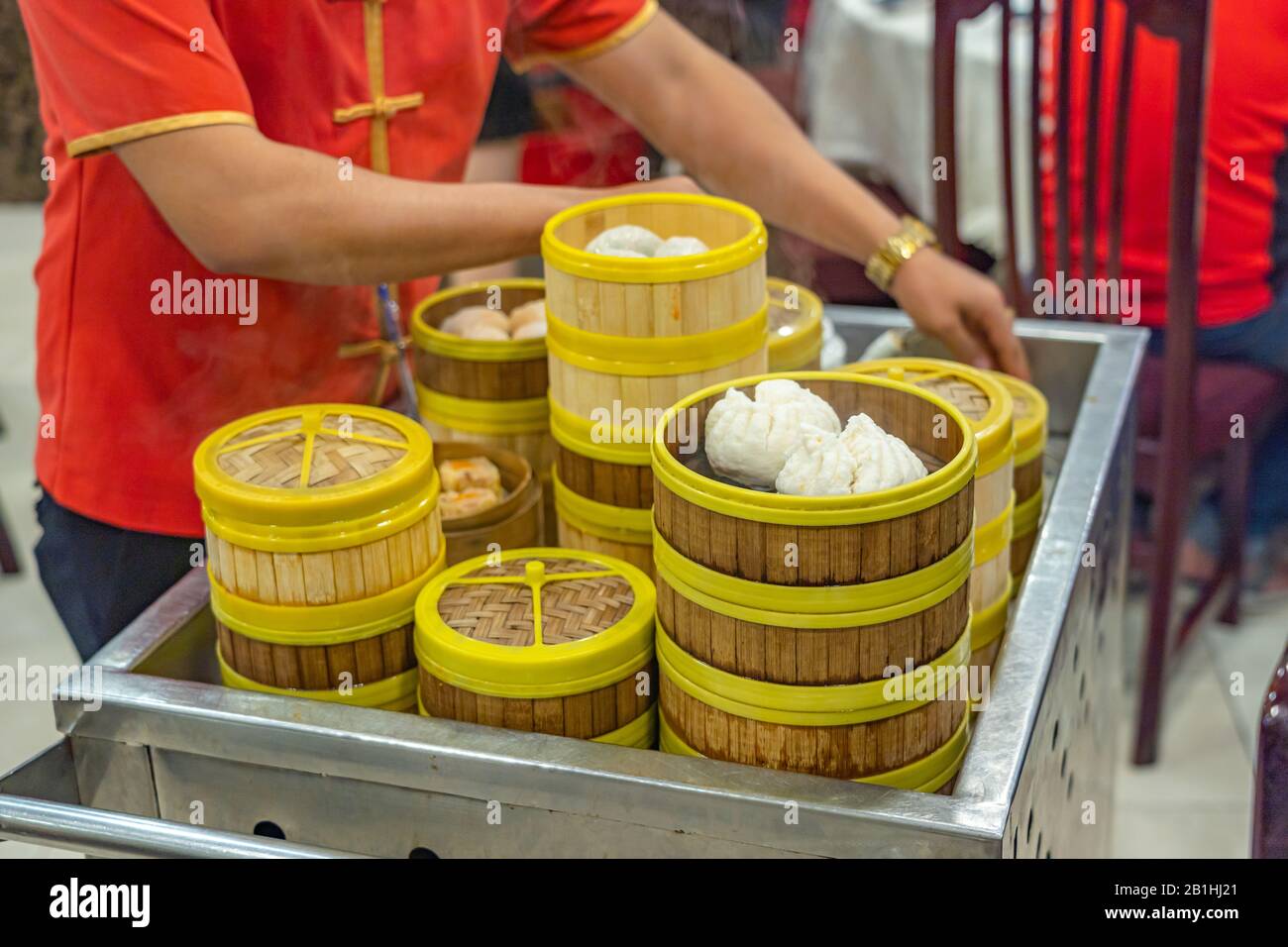 Cameriera in costume cinese che serve dimmum in scatole di bambù steamer Foto Stock
