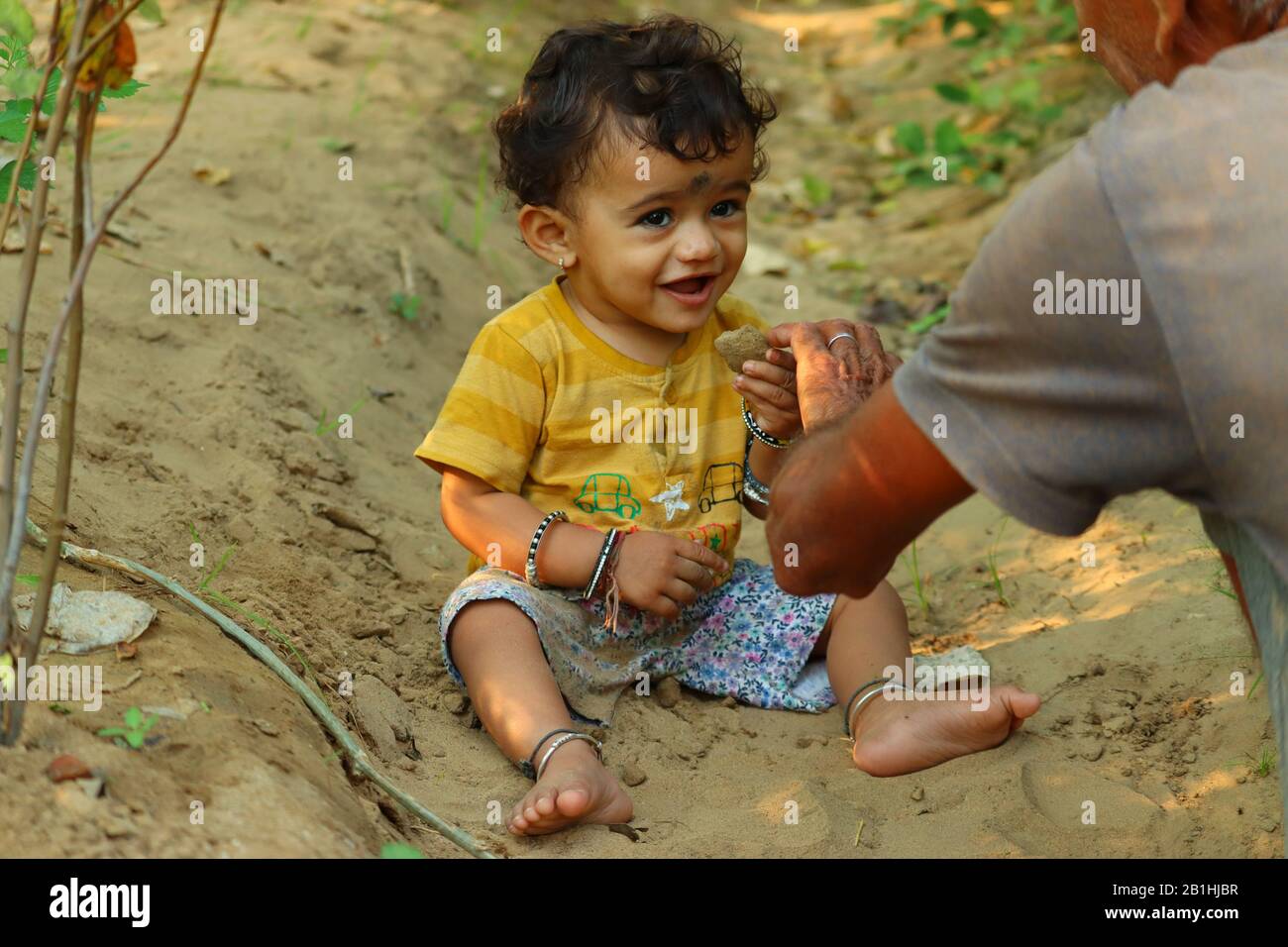 Ritratto all'aperto di un bel bambino asiatico o indiano carino con felice sorridente espressione facciale giocare con sabbia e guardare la natura e mostrare ciò che Foto Stock