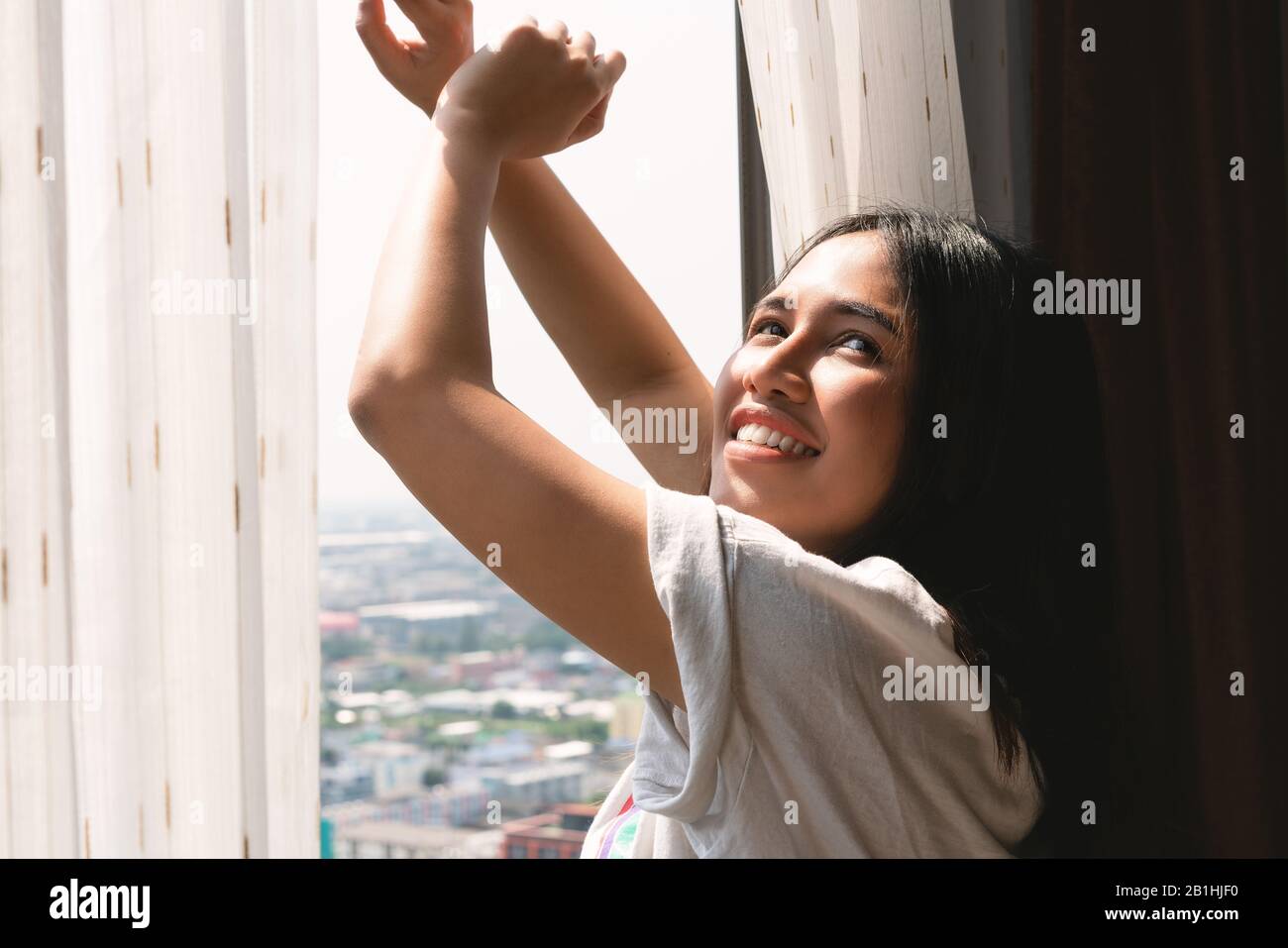 Giovane donna diversa sbadigia e stretching fuori dalla finestra di blocco appartamento - testa Sleepy stanco millennial ragazza asiatica svegliarsi tardi al sole di mattina luminoso - Weekend, concetto pigro e fresco Foto Stock