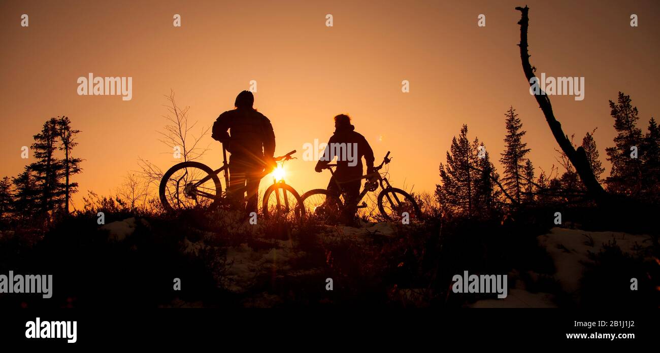 uomo e donna in piedi con una bicicletta in silhouette dal tramonto Foto Stock