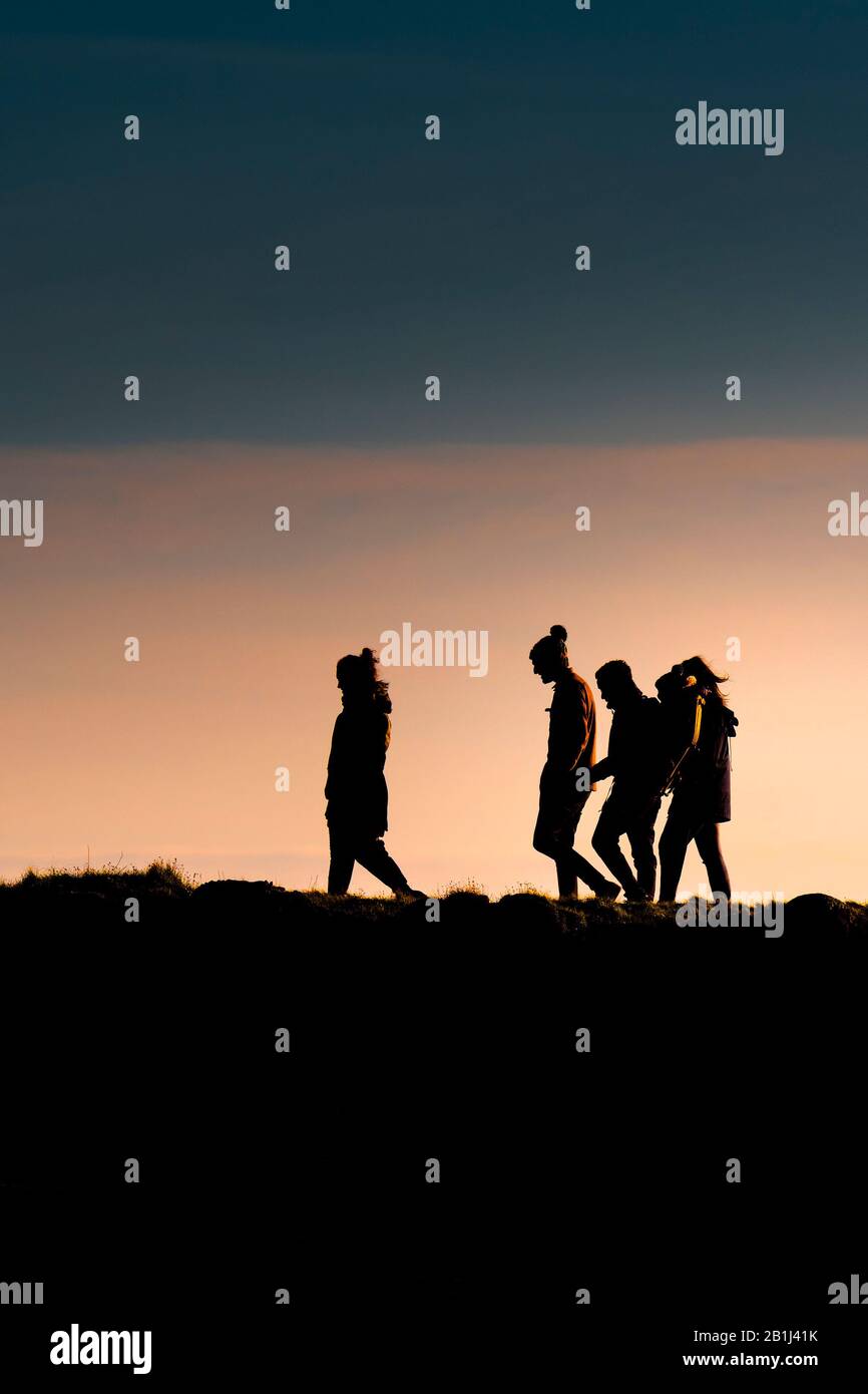 Un gruppo di amici che camminano a casa mentre il sole tramonta alla fine della giornata. Foto Stock