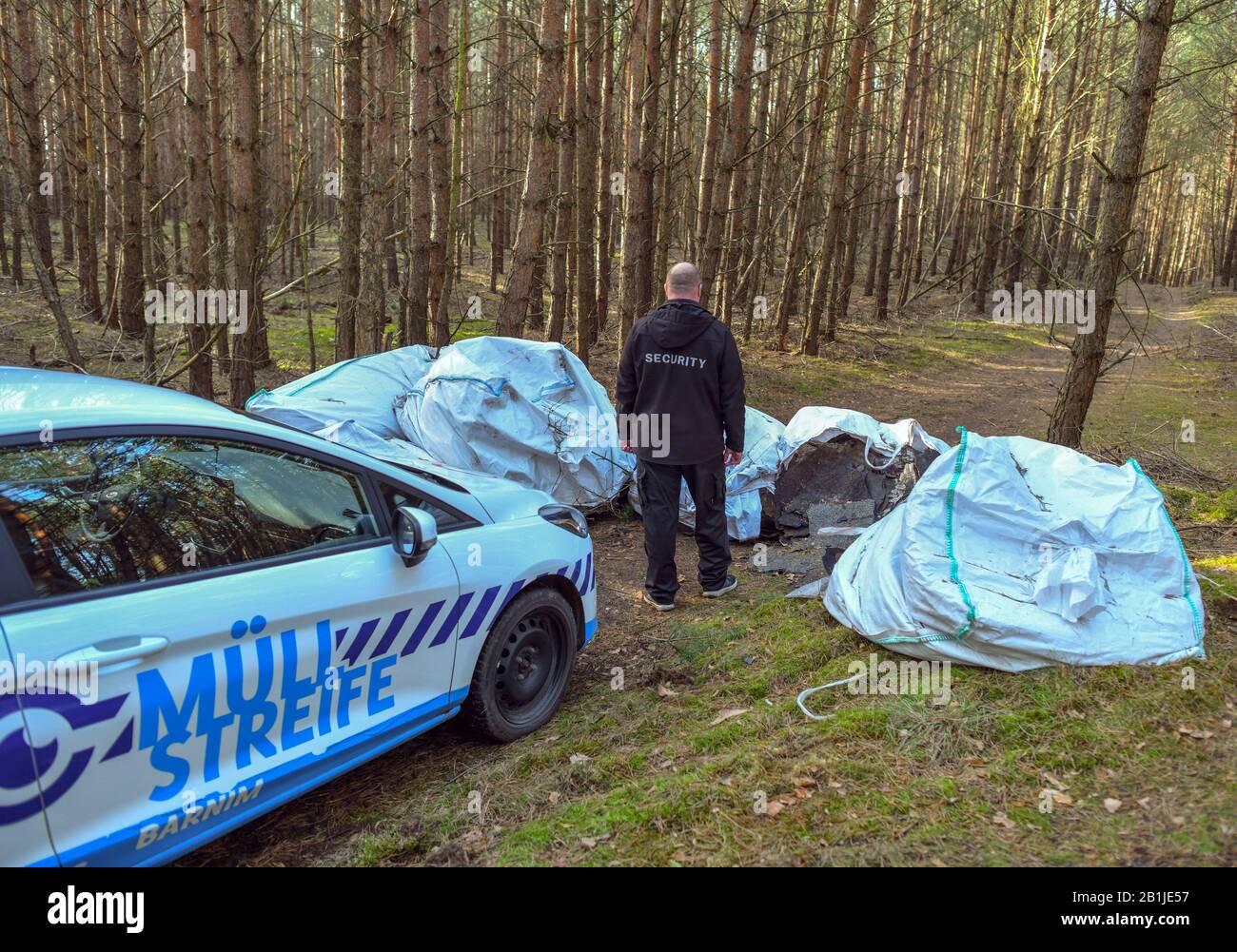 13 febbraio 2020, Brandenburg, Groß Schönebeck: Un dipendente della Platz Sicherheits GmbH per conto della Barnimer Müll-Streife si trova in una foresta di fronte a grossi sacchi di copertura e altri macerie. Il Brandeburgo ha un crescente problema di rifiuti illegali. In particolare, i rifiuti pericolosi, tra cui macerie edili, atterra in campagna su larga scala di notte e in nebbia. Al Barnim, una pattuglia dei rifiuti sta cercando di rintracciare gli autori. I primi risultati sono già disponibili. Foto: Patrick Pleul/dpa-Zentralbild/ZB Foto Stock