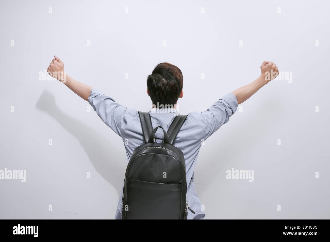 Vista posteriore di un uomo casual che celebra il successo con le mani in aria su sfondo bianco Foto Stock