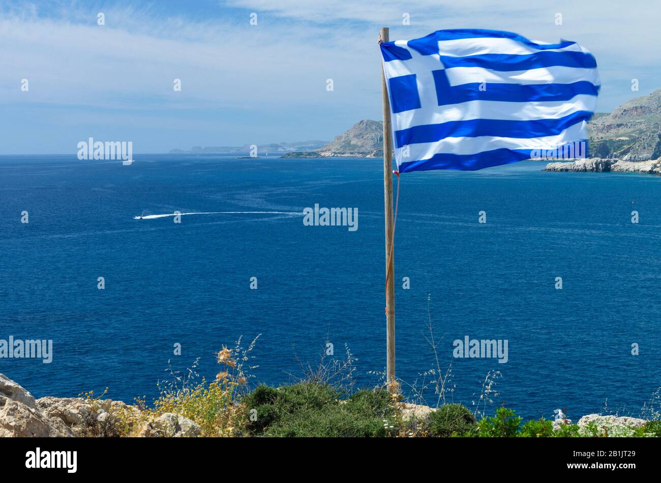 Bellissimo paesaggio mediterraneo con una bandiera greca che vola al vento in una giornata di sole (Rodi, Grecia) Foto Stock