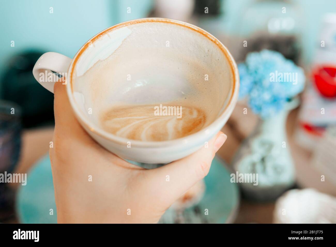 Elegante tazza in porcellana bianca semi-vuota con cappuccino, i resti di schiuma sulle pareti della tazza. Mangiare in un bellissimo caffè in colori menta Foto Stock