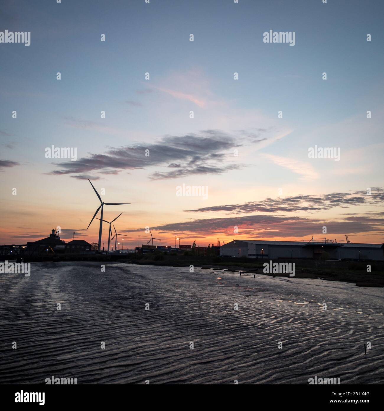 Crepuscolo al Porto di Tilbury, Essex, Regno Unito. Vista al tramonto della bassa marea del Tamigi e delle turbine eoliche che girano sullo sfondo. Foto Stock