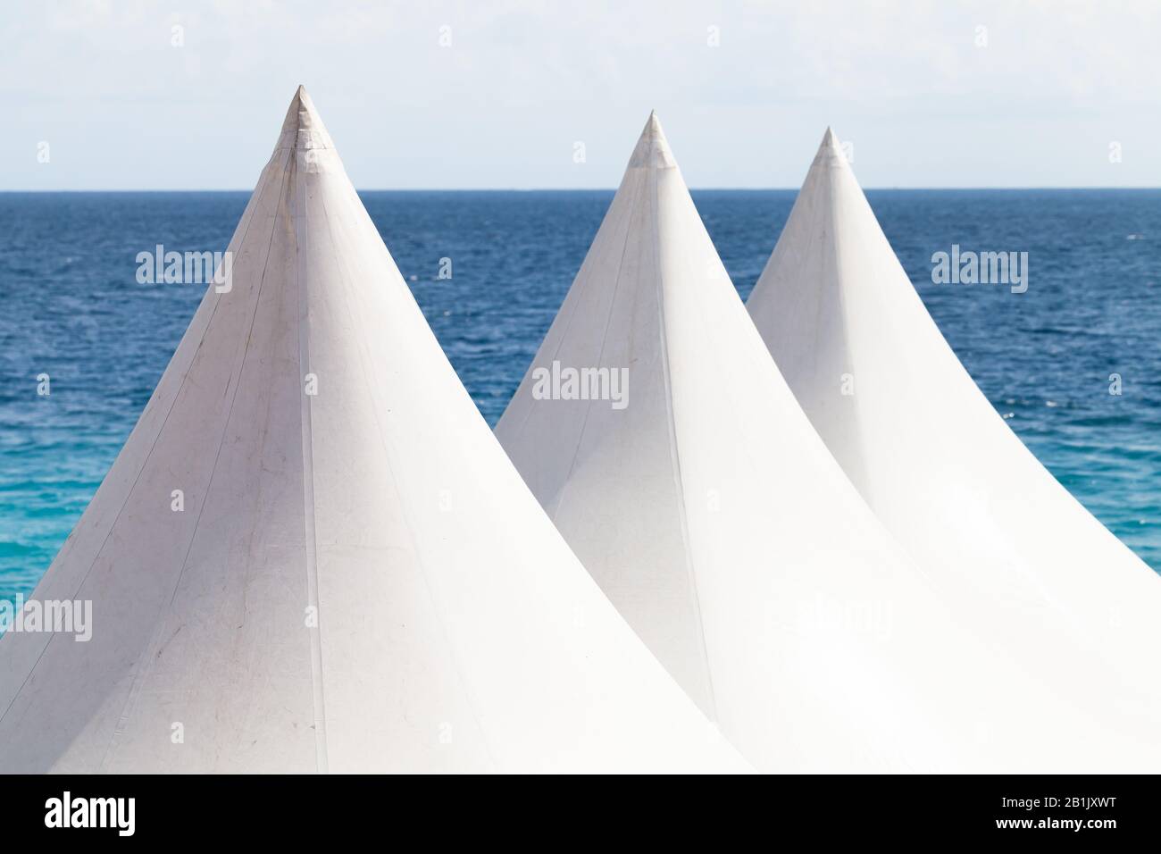 Tende bianche sotto un cielo blu brillante con acqua di mare su uno sfondo Foto Stock