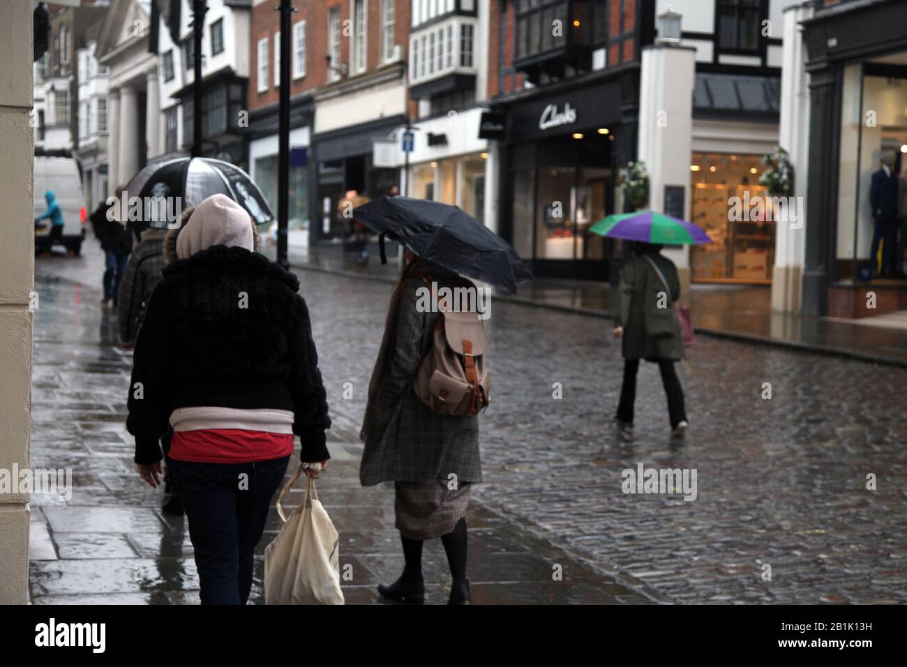 Pedoni e acquirenti che camminano sotto la pioggia facendo shopping con ombrelloni lungo Guildford High Street, Guildford, Surrey, UK - Foto Stock