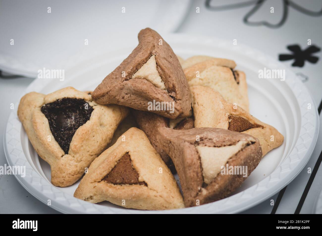 Hamantaschen. (ozen haman). Cibo ebraico per Purim. Pasta croccante triangolare, farcita con datteri, halva e cioccolato, su una piastra bianca. Foto Stock